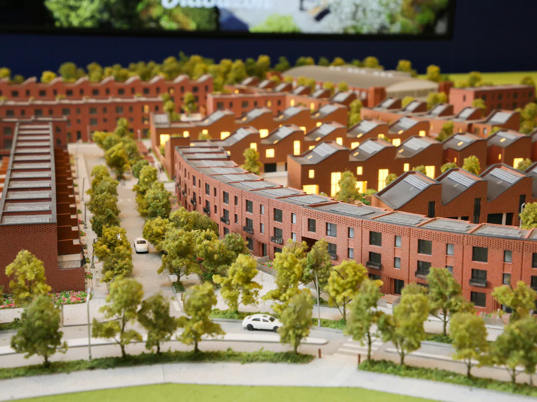 Detailed architectural model of Brabazon, featuring curved brick townhouses, tree-lined streets, and illuminated windows, with cars and greenery