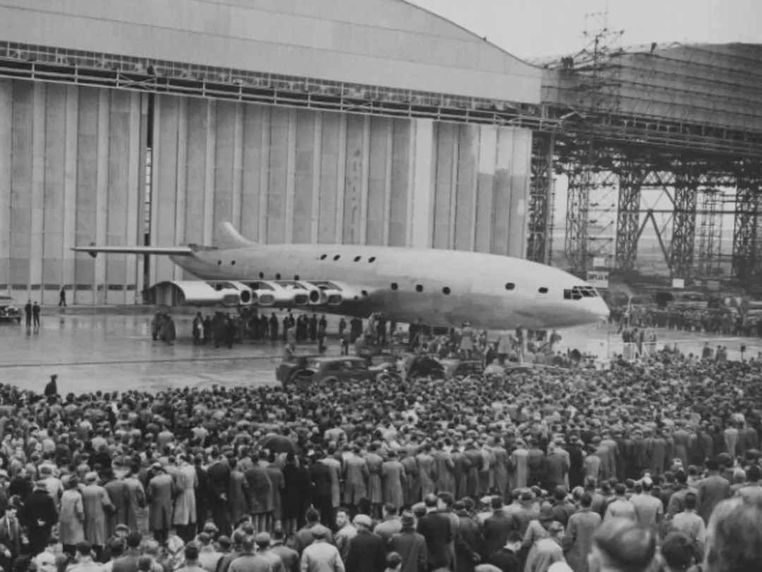 Historic image of a large crowd gathers in front of Brabazon aircraft parked outside an industrial hangar at Filton Airfield. 