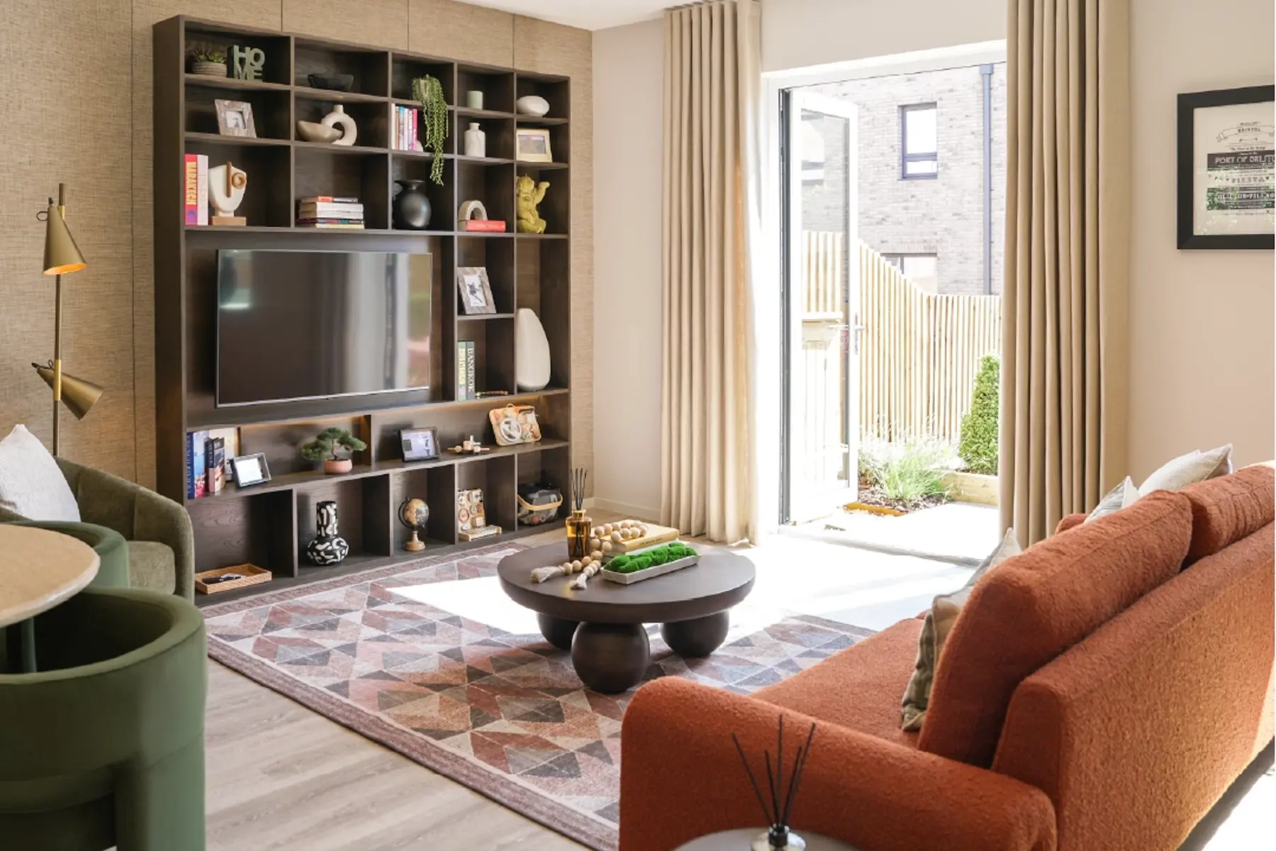 Modern living room featuring a custom TV shelf, orange sofa, patterned rug, and natural light streaming in through open doors.