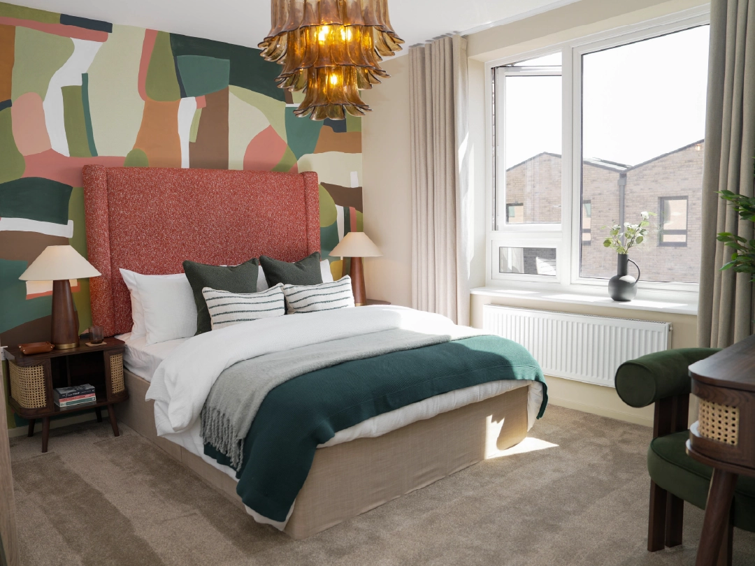 A stylish primary bedroom at Brabazon, featuring a textured orange headboard, colourful mural, cozy bedding, and a large window with natural light.