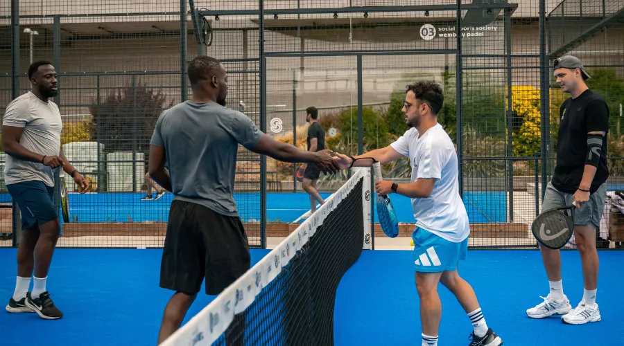 Group of men in sportswear shaking hands over a net at the end of a Padel game.