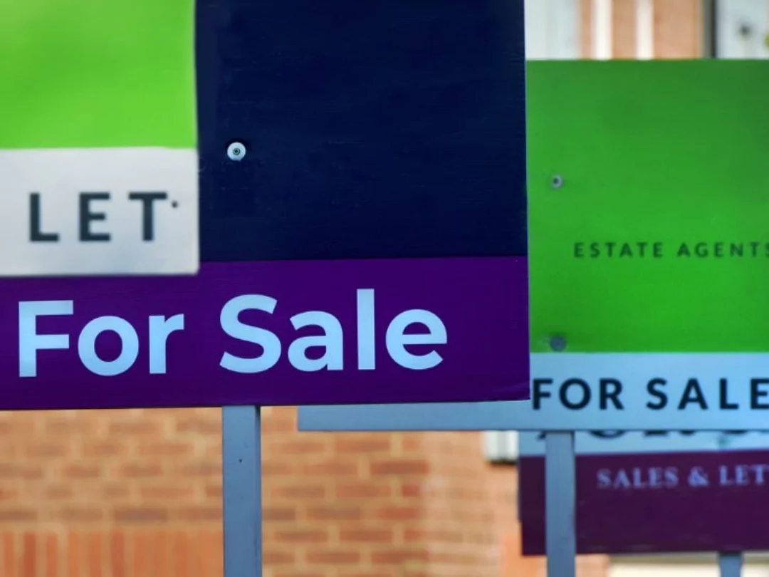 Close up row of 'For Sale' signs in a street of brick homes. 