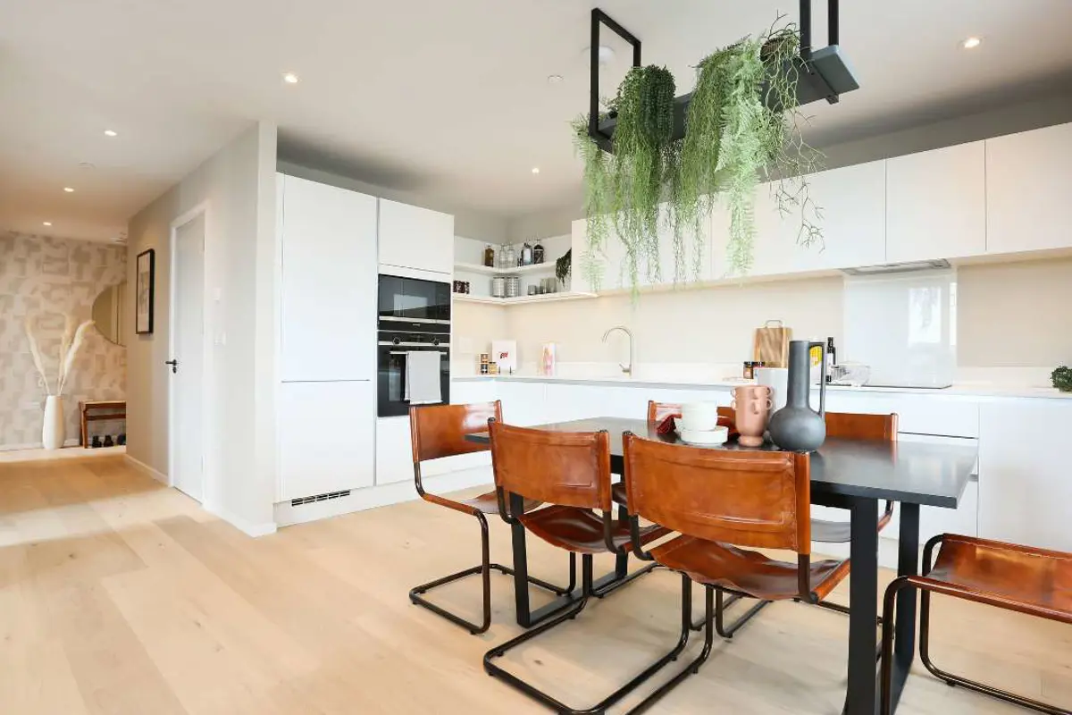 Open-plan kitchen diner with glossy white work tops, hanging plants and stylish seating.