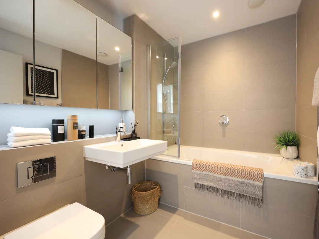 A wide angle of the family bathroom with added extras such as the large mirrored storage units and faux plants.