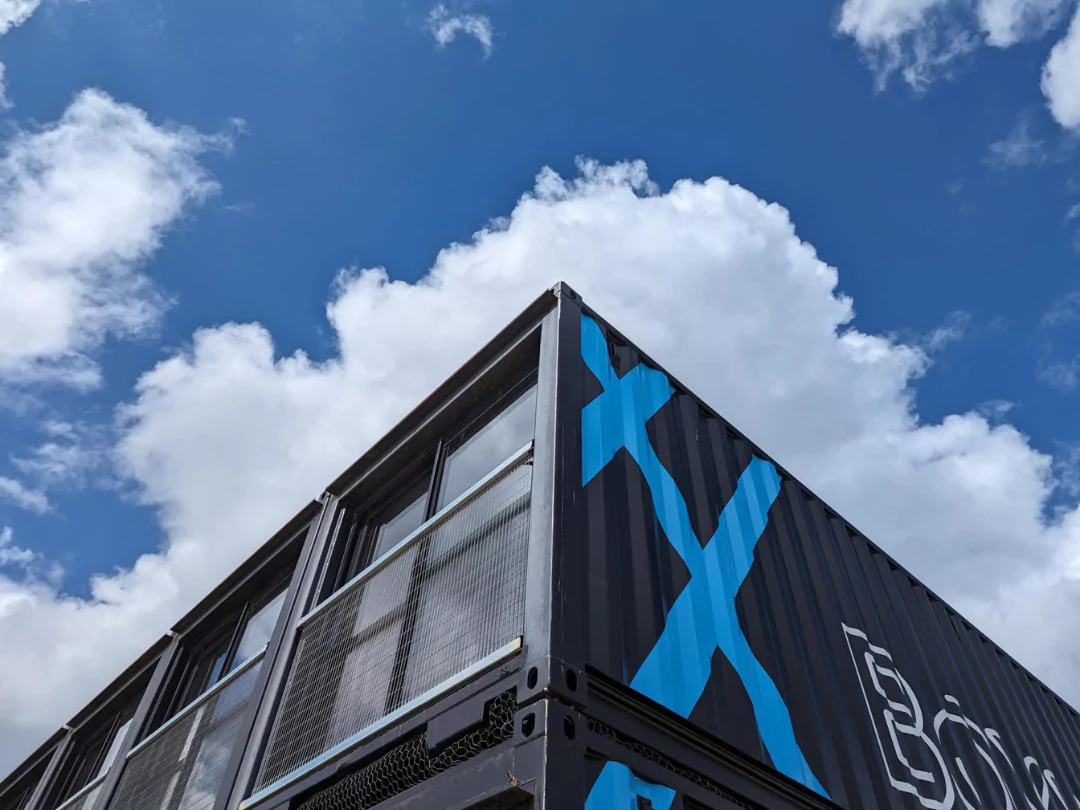 A blue and black container office building stands against a clear blue sky, showcasing modern architecture.