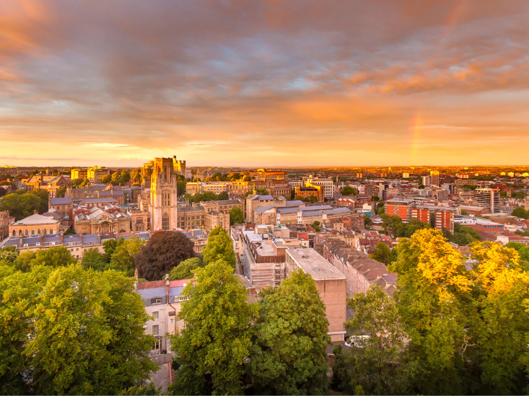 Rooftops and treetops of the city of Bristol bathed in orange sunlight in the late afternoon.
